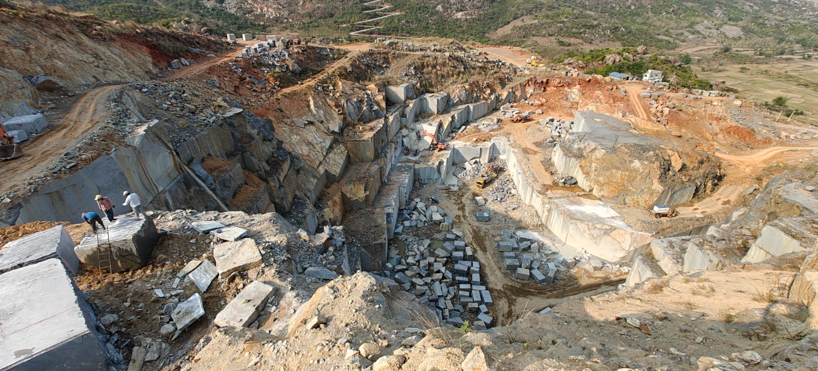 Aerial panorama of the Pristine Impex Silk Blue granite quarry, with cut benches, blocks and workers on the quarry face