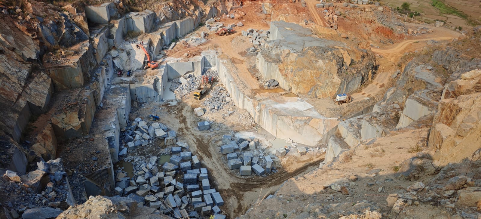 Excavators working the floor of the Silk Blue granite quarry among freshly cut blocks